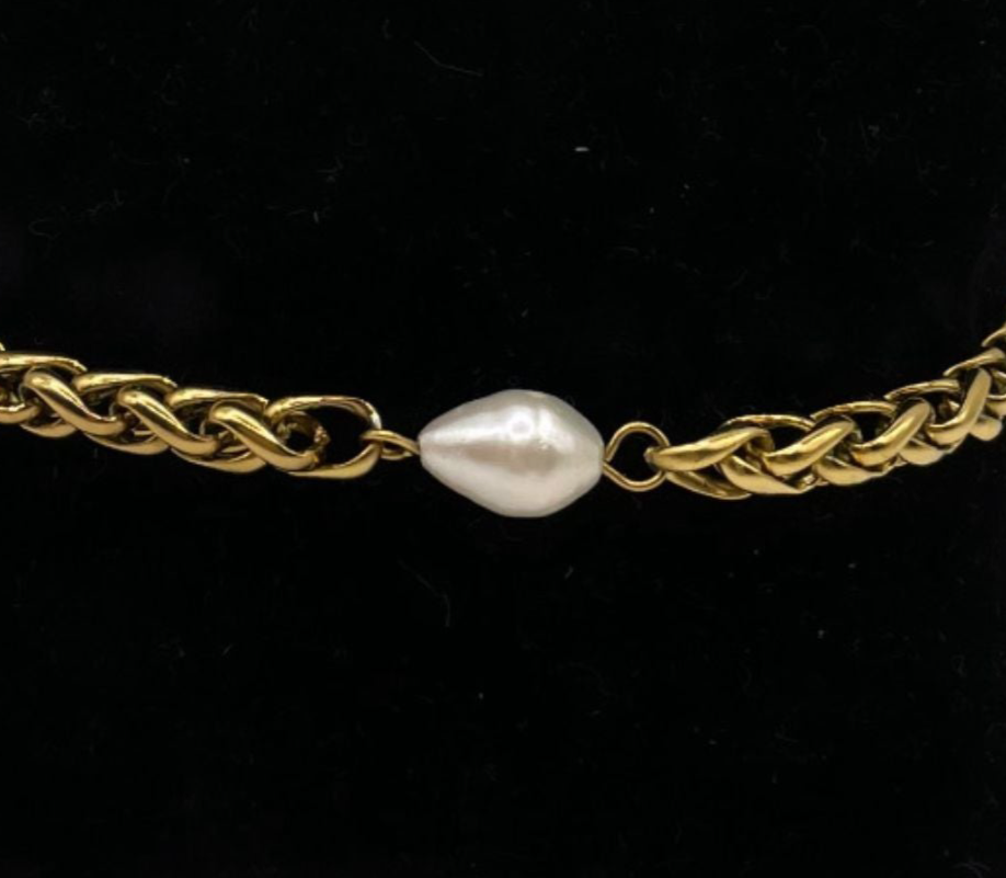 Pulsera dorada con eslabones y perla central, mostrada junto a otras cadenas doradas.