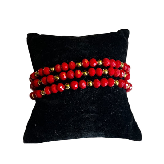 Pulsera roja hecha a mano conbalines dorados, presentada sobre cojín negro. Joyería artesanal de Aura’s.