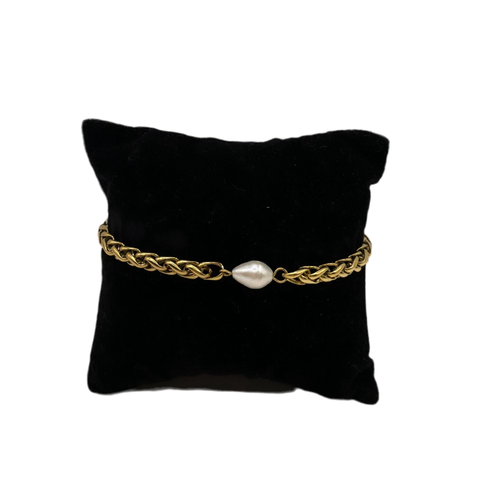 Brazalete dorado con perla al centro, sobre cojín de exhibición.